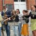 "Des musiciens de l’Ensemble Instrumental Waremmien jouent dans la rue à Bleret, avec des flûtes traversières et saxophones devant un public curieux, lors du concert-apéro du 6 juillet 2025."